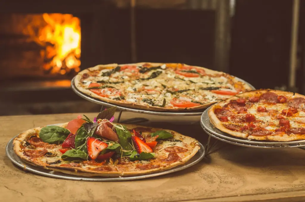 Acasă Trei pizza proaspăt coapte pe suporturi, în fața unui cuptor cu lemne aprins
